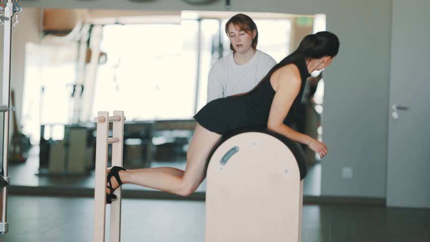Young woman training with her personal coach in a modern pilates studio on specialized equipment