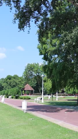 Wide park walkway on a sunny day with wooden pavilion and green trees