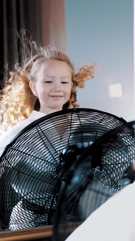 Hair fluttering in the wind. close-up, cute little girl is having fun.She stands in front of the fan, the air flows her curly hair, as if in the wind