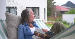 Senior woman sitting up after glancing toward yard, returning to reading book on hammock for rest. Poolside, patio, garden, outdoor, relaxation, serene, leisure - Powered by Shutterstock - Get 15% off with code: PIKWIZARD15