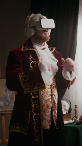 Vertical shot of young male aristocrat in baroque coat immersing in virtual reality wearing augmented wireless headset in classical studio with abstract painting in background