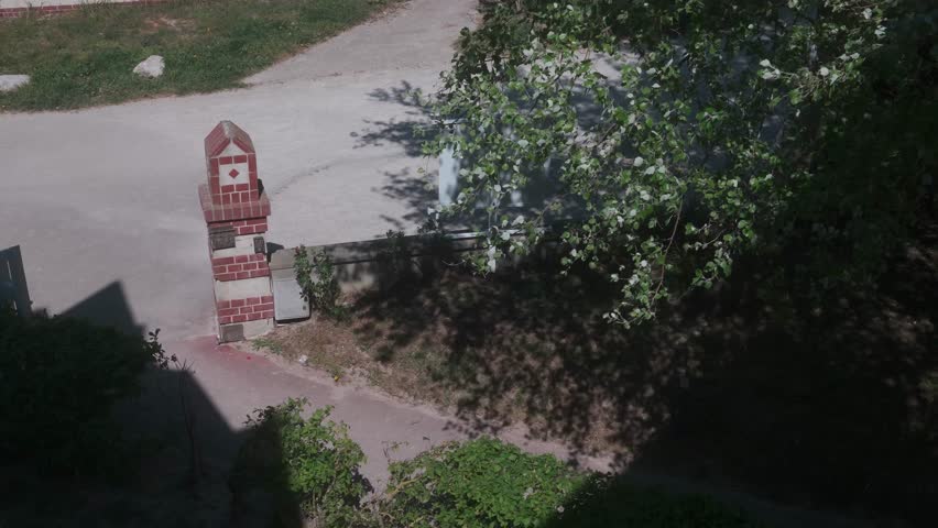 High angle view of a quiet street corner and brick gate near the seafront at Le Crotoy, France, while strong wind blows through the tree.