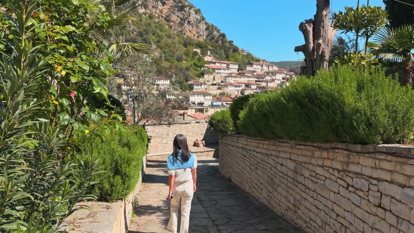 Woman tourist walk sightseeing old Gorica quarter residential district in Berat. Tiered Ottoman narrow old cobblestone streets in sunny summer day in Albania