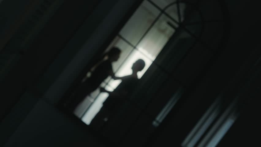 Silhouettes of a quarrelling couple in a dark room, reflected in a mirror. Aggressive gestures and conflict between partners, a concept of relationship problems and family tension. High quality 4k