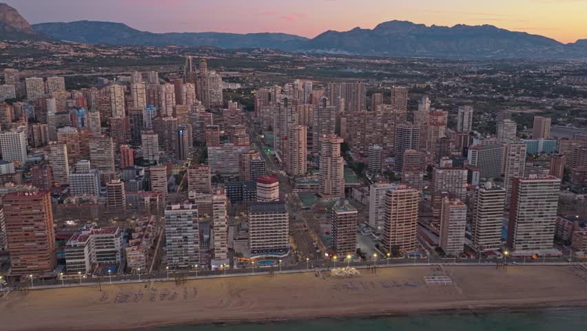 Majestic aerial view flying over the benidorm skyline in spain. Beautiful cityscape with skyscrapers along the coastline at sunset
