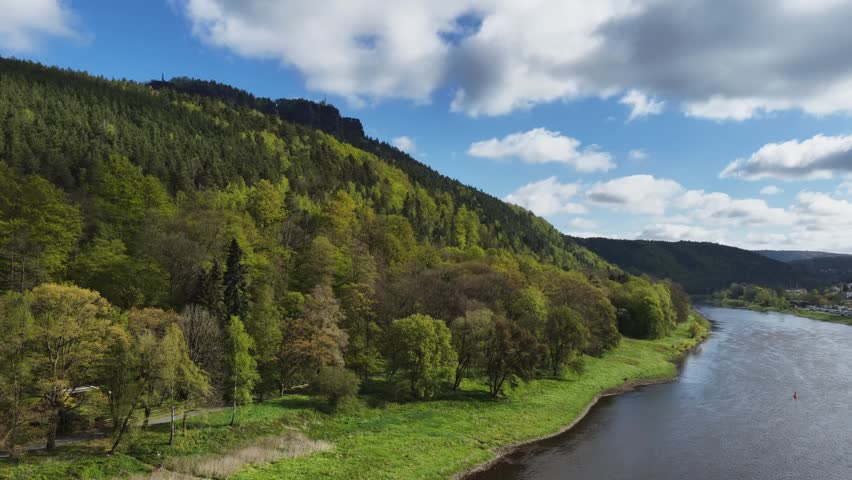 Scenic aerial view of the Elbe valley in Saxon Switzerland with densely forested hills and the Elbe river under a blue cloudy sky in spring.
