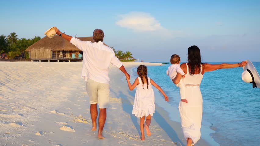 Slow motion view of a happy family on holidays running on a tropical paradise beach in the Maldives islands during sunset time