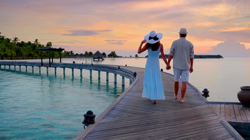 A couple walks holding hands over a pier in the tropical Maldives islands during their romantic vacations