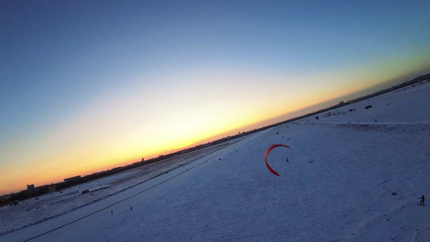 Aerial FPV view of the vast snow-covered Tempelhofer Feld at sunset, with a vibrant sky contrasting with the icy white terrain, Berlin, Berlin, Germany.