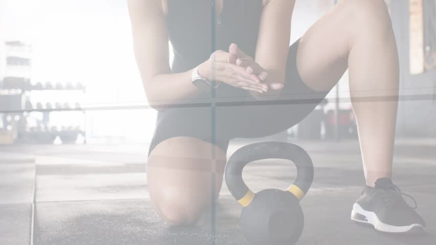 Woman kneeling on rubber floor rubbing hands and gripping kettlebell, preparing to lift for fitness. Gym, weights, athlete, training, equipment, rack, action