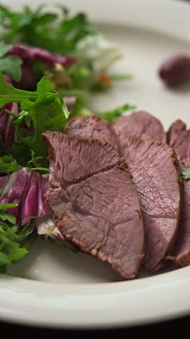 Close view of gravy poured onto lamb roast slices served with fresh salad on a plate.