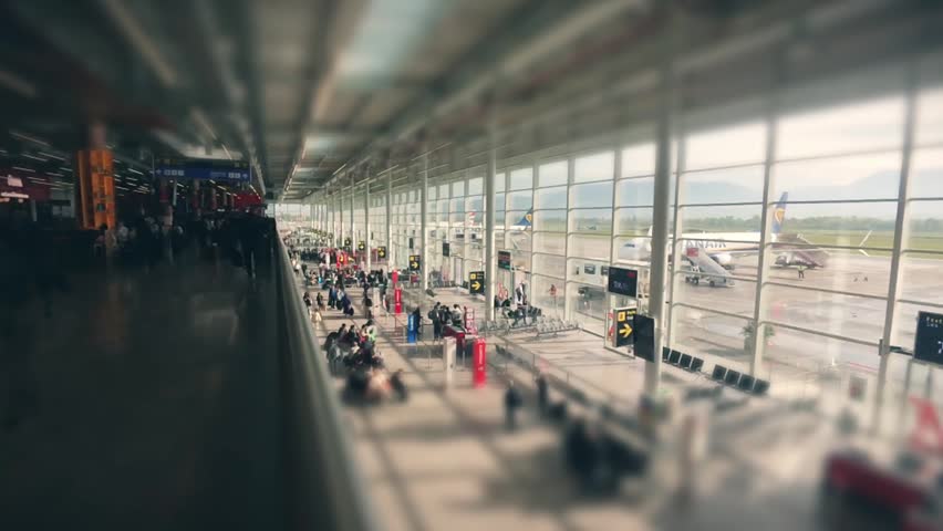 Tirana, Albania - 15th april, 2026: timelape zoom in bustling modern airport terminal with passengers sit waiting by gates.Flight cancellation interruption concept. Miniature tilt-shift effect blur.
