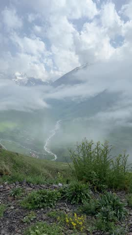A foggy high-altitude landscape. Aerial view through clouds and fog over a green valley of mountains and slopes in North Ossetia, gently floating above the mountainous landscape. Beauty, epic scale, inspiring