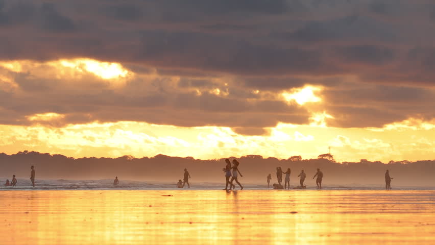 Cinematic sunset over a tropical beach in Costa Rica with golden reflections on wet sand and silhouettes of people enjoying the ocean under a dramatic sky
