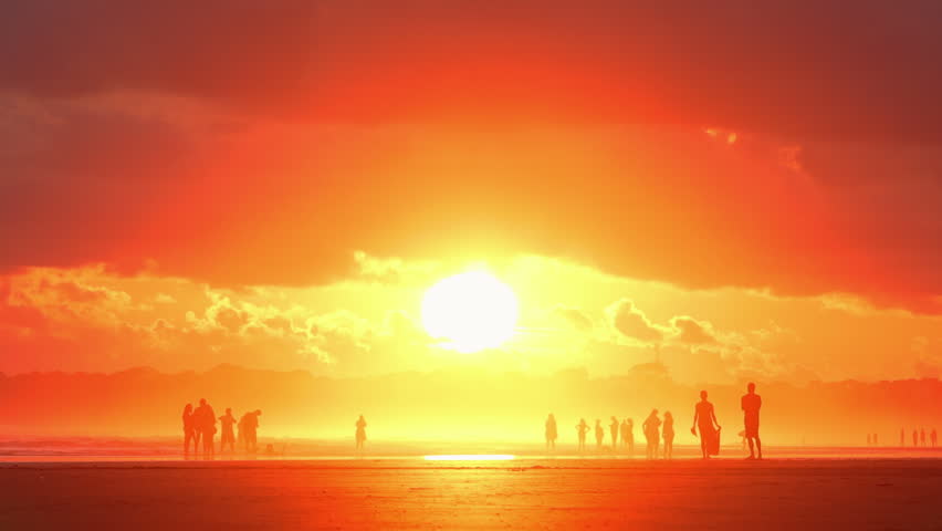 Stunning golden sunset over a tropical beach in Costa Rica with a massive bright sun disc and silhouettes of people walking on the shore during the golden hour