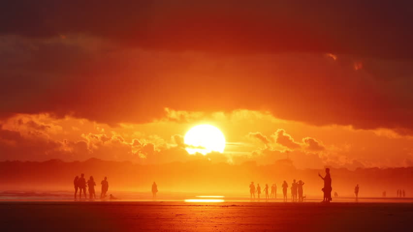 Stunning golden sunset over a tropical beach in Costa Rica with a massive bright sun disc and silhouettes of people walking on the shore during the golden hour