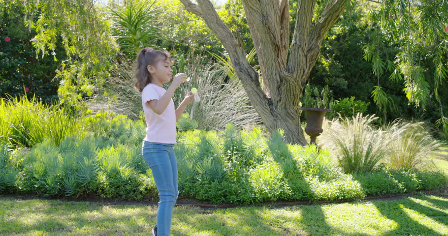 Child (female) holding bubble wand and bottle, blowing and popping bubbles on sunny lawn for fun. Backyard, garden, outdoors, sunlight, kid, girl, play