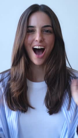 Energetic young brunette woman with long hair looking directly at the camera, talking, smiling, and gesturing with her hands, enthusiastically communicating against a plain white background