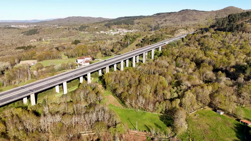 Elevated highway bridge crossing a lush green valley with forests and scattered houses