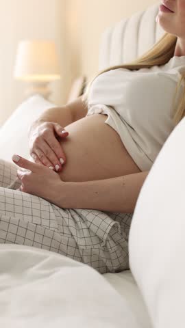 Pregnant woman touching her belly on bed at home, closeup. Camera moving in