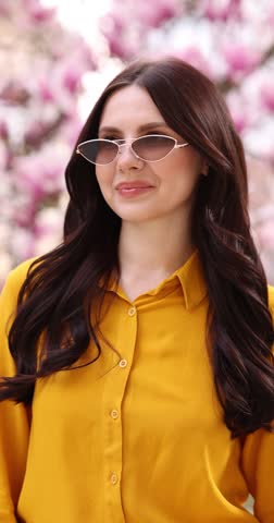 Beautiful woman wearing stylish sunglasses in park with blossoming magnolia trees