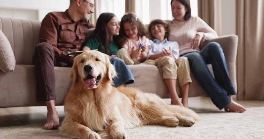 Large family with children relaxing on couch in living room, golden retriever dog lying on floor, kids playing games using smartphone, interacting with parents, having fun online on leisure at home