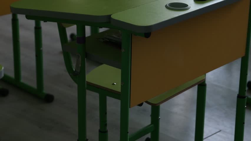Green desks and chairs in classroom at school, closeup. Camera moving up and right