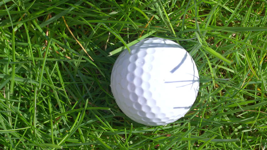 Close up of a golf ball on grass, with a golf club close by, aiming to hit the ball a few times and finally hitting the ball.