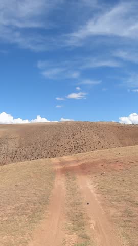 Vertical video of a car driving along a country road under blue sky. Altai desert and semi-desert environment.