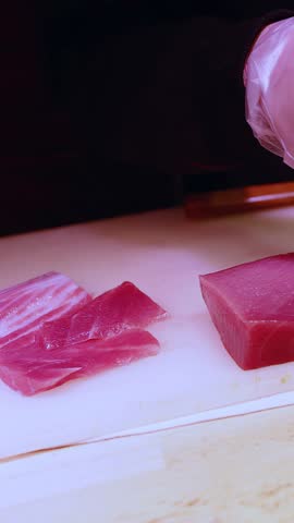Close-up of gloved hands slicing raw bluefin tuna for sashimi in a Japanese kitchen