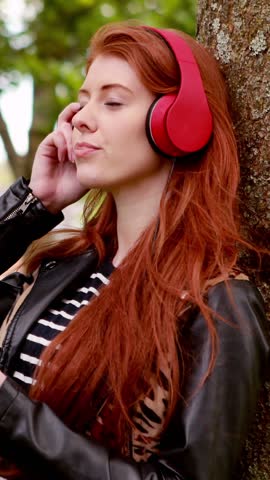 Pretty redhead listening to music in the park on a sunny day