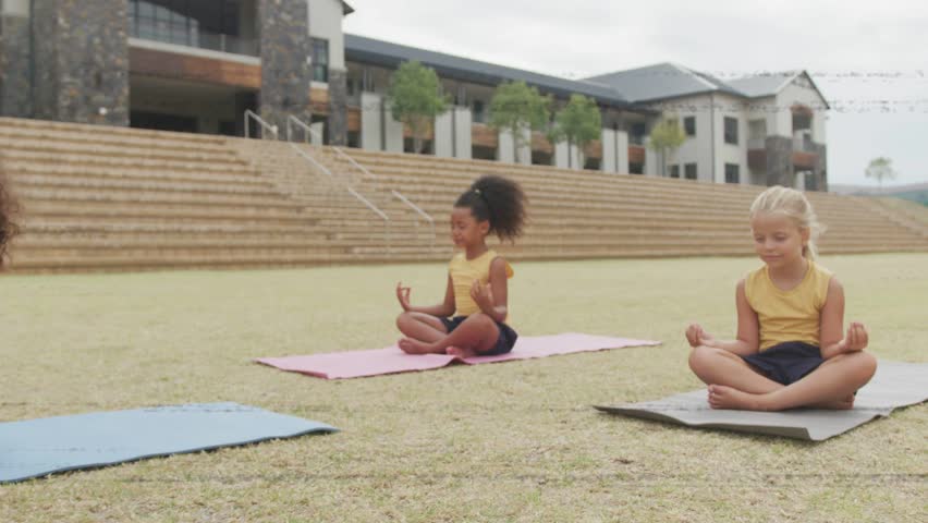 Four girls sitting yoga mats, fourth advancing, color bands clearing, camera zooming for wellness. Campus, outdoor, students, meditation, calm, focus, lawn
