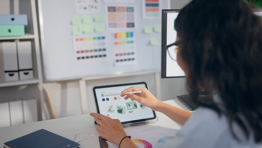 Young Hispanic woman designer sitting at her desk, working in an office. Attractive businesswoman focusing on creative work while enjoying a calm and productive moment in a modern company workspace.