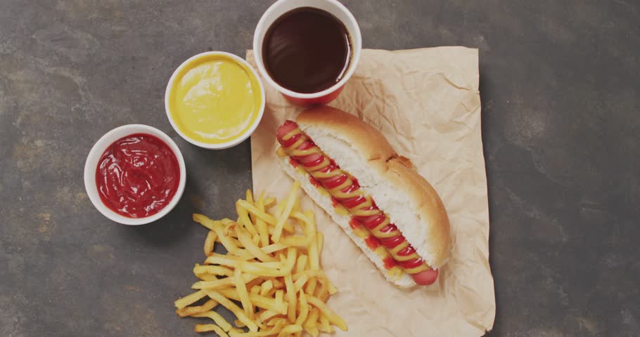 Hot dog staying centered while labels popping, sliding, highlighting sausage and fries for menu ads. Bun, condiments, overhead, flatlay, potato, beverage, texture