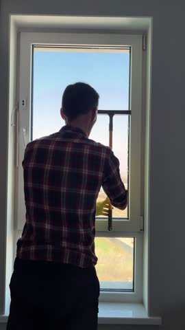 Rear view of a man cleaning a large window glass in a house with a scenic view of the street