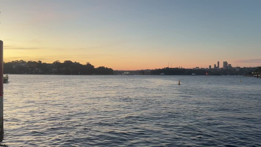 Serene sunset view over the water in Sydney with the city skyline in the distance.
