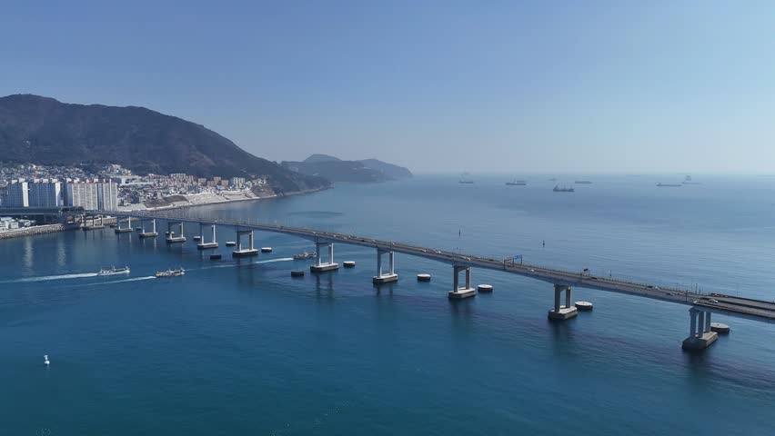 Aerial view of coastal bridge over blue sea in Busan, South Korea. Maritime transport, urban infrastructure and shipping routes across coastal city landscape.