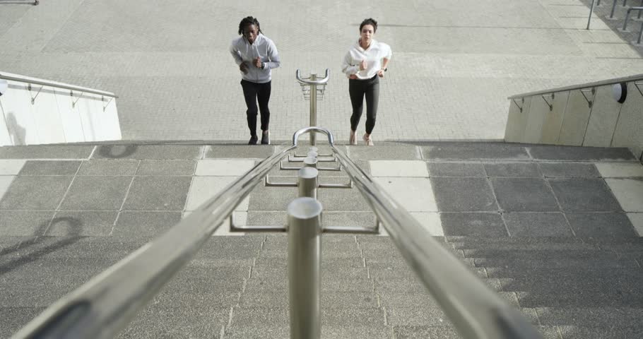 Diverse friends jogging toward stairs at plaza running up steps pivoting toward camera for fitness. Athletic, teamwork, vitality, urban, celebration, motivation, energetic