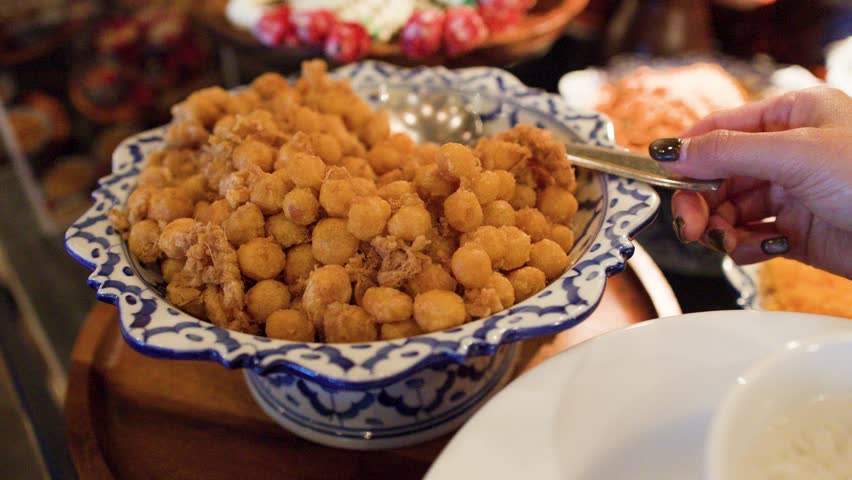 Close-up shot of a person scooping golden fried shrimp balls from a ceramic bowl