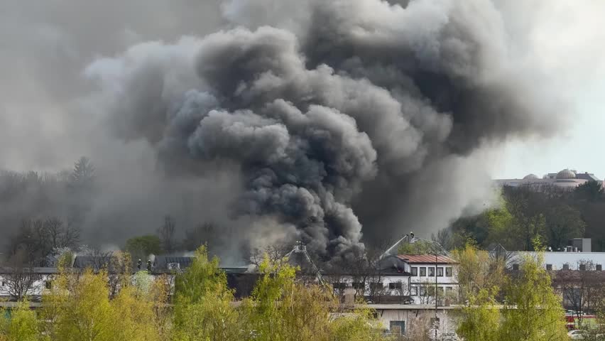 Firefighters battling large fire with flames and thick black smoke in Prague, Europe. Emergency response scene with rescue services controlling burning building and heavy smoke cloud in urban area