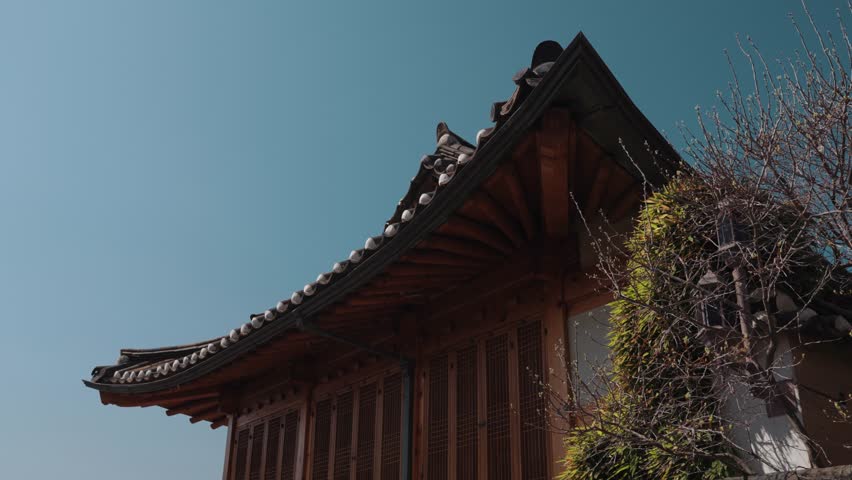 Traditional Korean hanok house architecture in Bukchon Hanok Village, Seoul, South Korea, featuring wooden details, curved tiled roof, and historic residential design under clear blue sky.