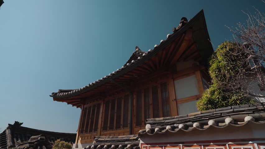 Traditional Korean hanok house architecture in Bukchon Hanok Village, Seoul, South Korea, featuring wooden details, curved tiled roof, and historic residential design under clear blue sky.