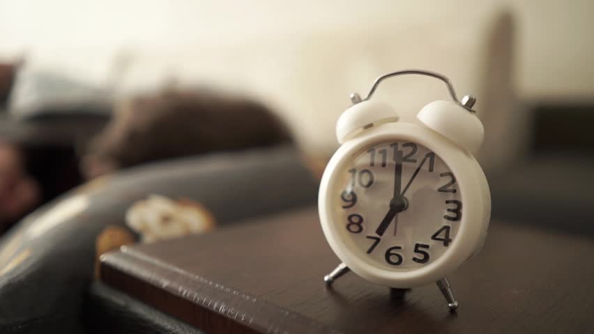 Fatigue, insomnia, man in bed with alarm clock waking him up due to burnout, exhaustion and fatigue in the bedroom.