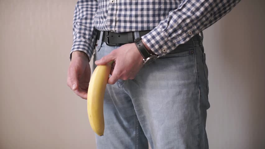 a man holds a banana in the groin area. Problems with the prostate. Age intimate problems of men. Steroids and potency. Passive lifestyle