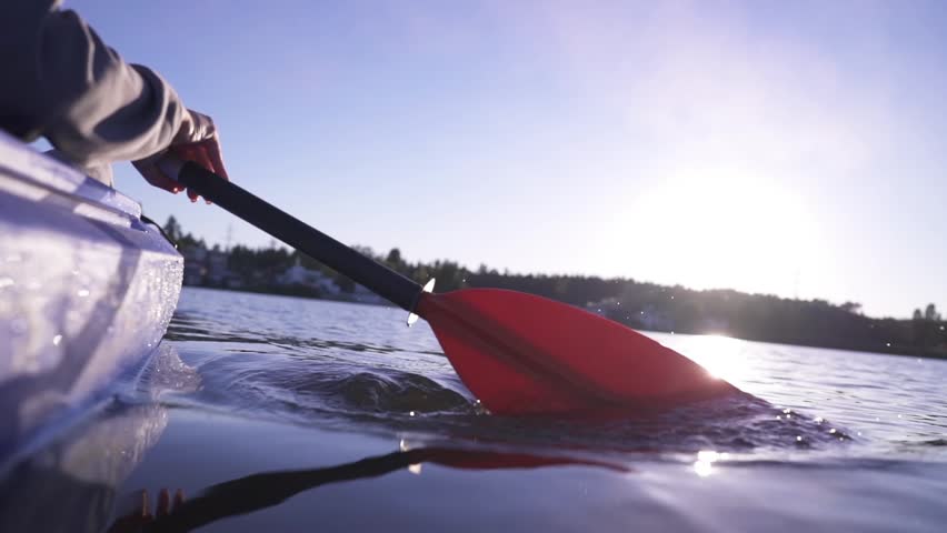 A woman paddles a kayak down a calm river. Active water recreation.