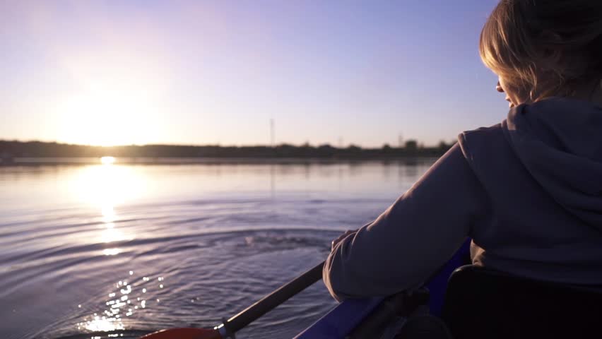 A woman paddles a kayak down a calm river. Active water recreation.