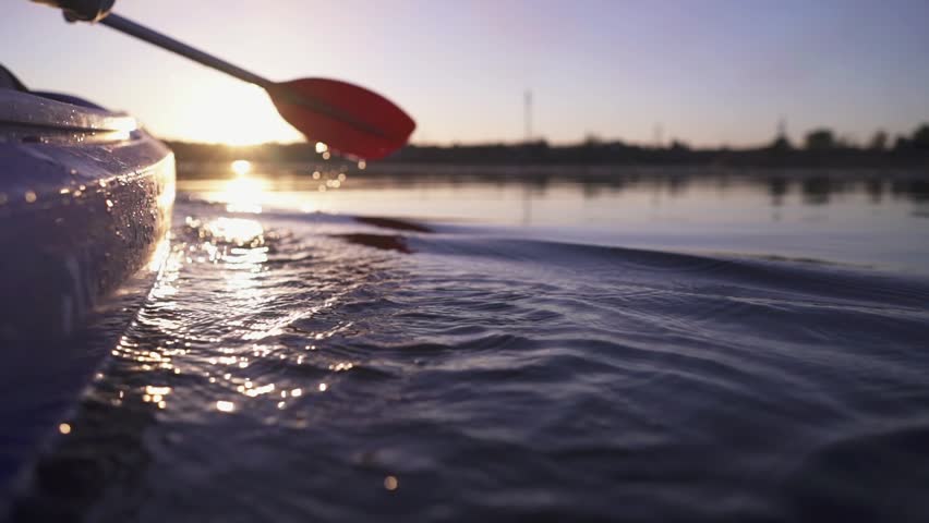 A woman paddles a kayak down a calm river. Active water recreation.