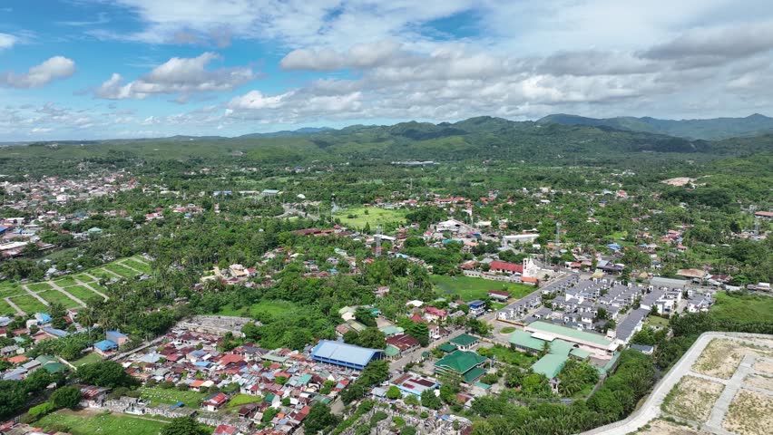 Land grabbing residential and commercial districts Danao Cebu Philippines mountain over populated population cluster of building and houses poor people squatter clear sky green trees mountain forest coastal sea ocean sailing fisherman boat ship aerial drone footage.