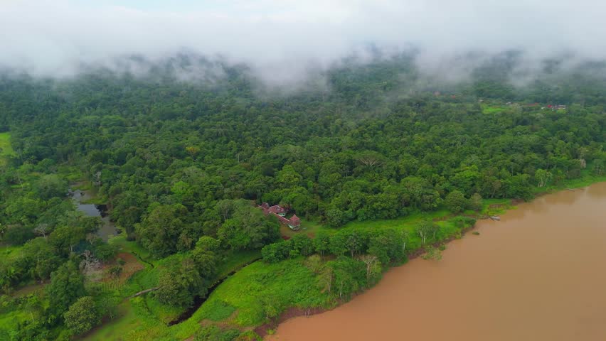 Aerial drone view of a hidden jungle retreat near Iquitos, Peru. The Amazon rainforest with a winding river surrounded by dense green forest.