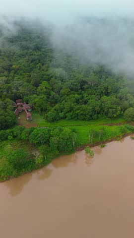 Vertical aerial drone view of a hidden jungle retreat near Iquitos, Peru. The Amazon rainforest with a winding river surrounded by dense green forest.